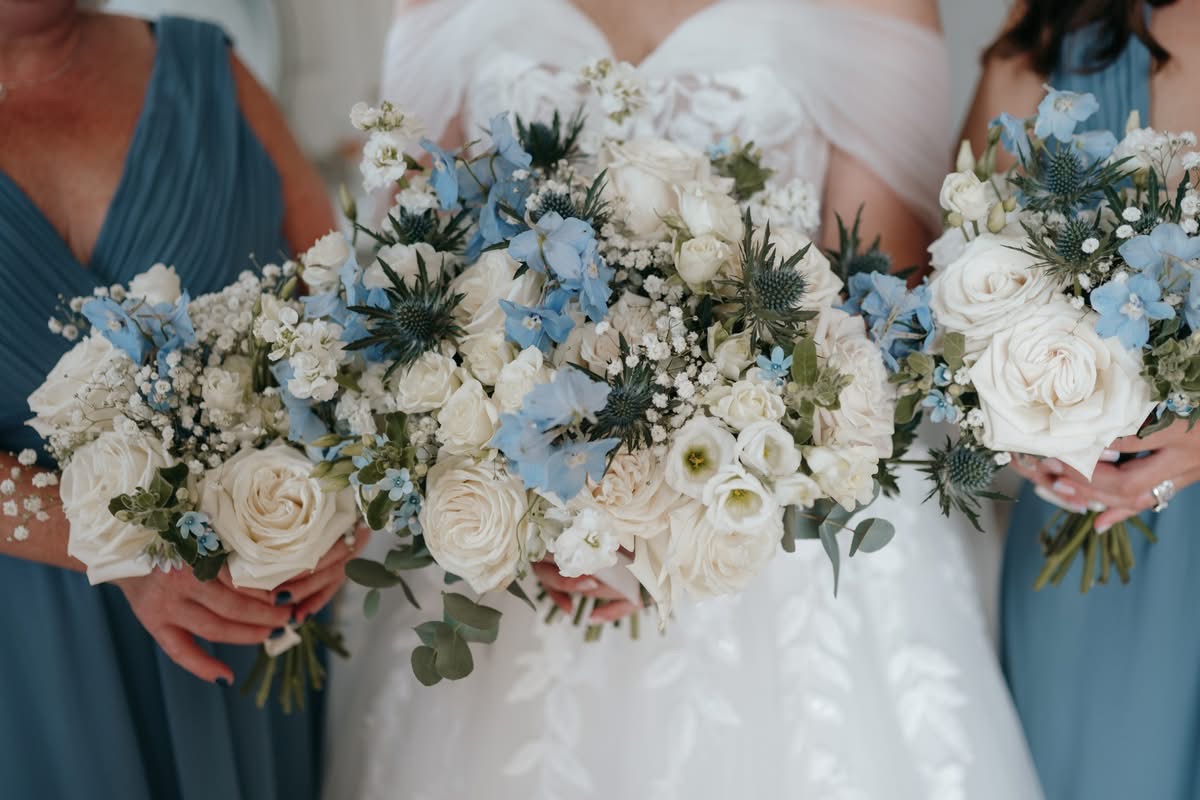 Three people in blue and white dresses hold bouquets of wedding flowers with white roses, blue blooms, and greenery—perfect for a stylish celebration at Doxford Barns in Northumberland.