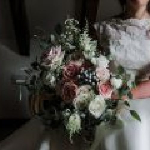 A bride in a white dress holds a large bouquet of pink, white, and green flowers, showcasing elegant wedding styling by a talented Northumberland wedding florist.