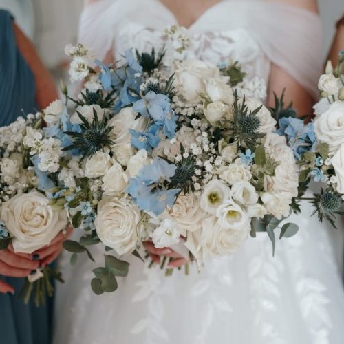 Three people in blue and white dresses hold bouquets of wedding flowers with white roses, blue blooms, and greenery—perfect for a stylish celebration at Doxford Barns in Northumberland.